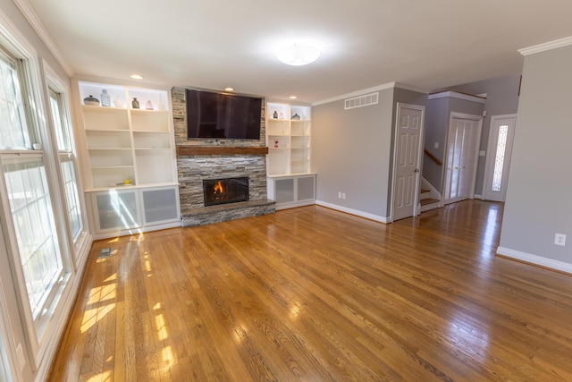 unfurnished living room with ornamental molding, a stone fireplace, stairway, and wood finished floors