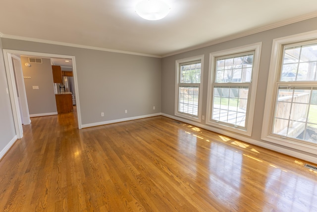 spare room featuring crown molding, wood finished floors, baseboards, and visible vents