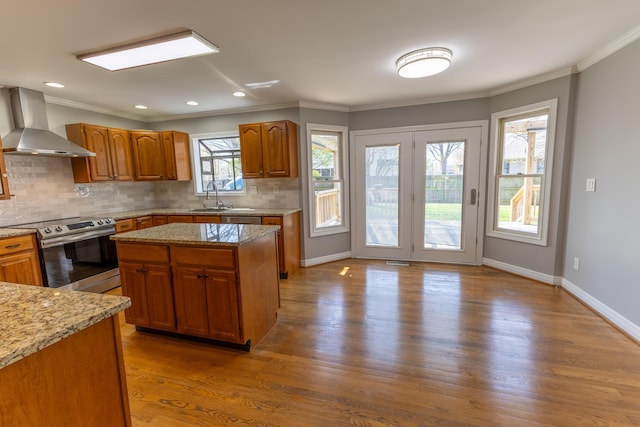 kitchen with wall chimney range hood, brown cabinets, appliances with stainless steel finishes, a sink, and wood finished floors