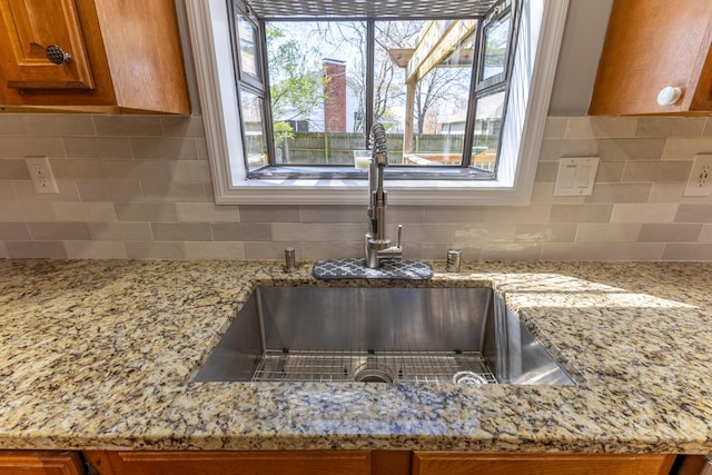 details featuring brown cabinets, a sink, backsplash, and light stone countertops