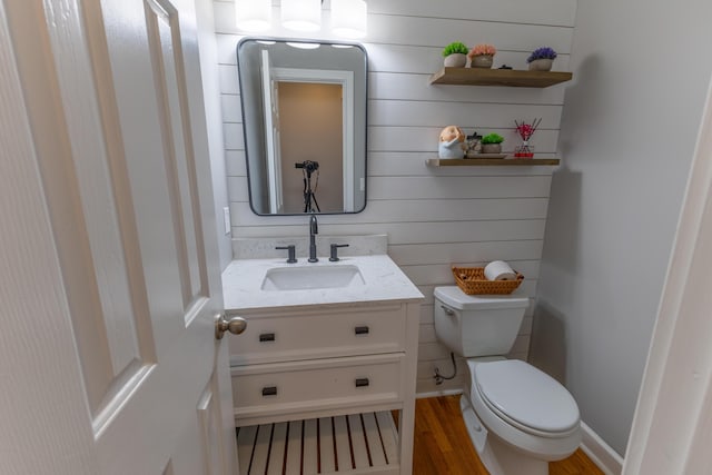 half bathroom with vanity, baseboards, toilet, and wood finished floors