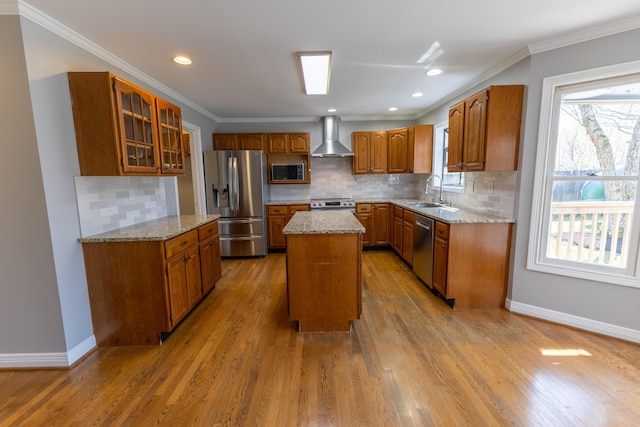 kitchen featuring crown molding, brown cabinetry, wall chimney range hood, appliances with stainless steel finishes, and a sink