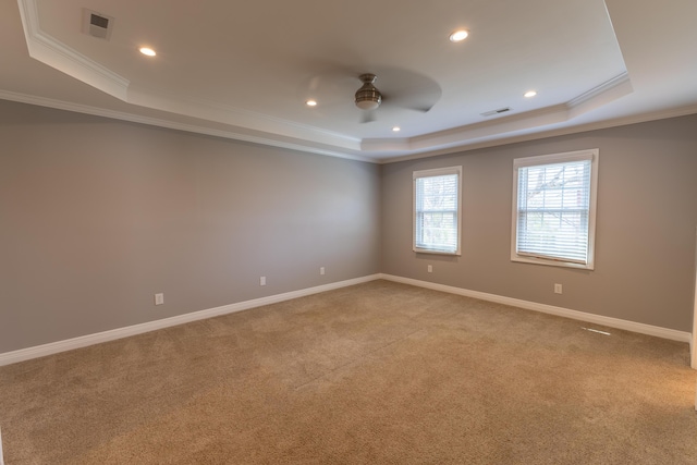 empty room featuring a raised ceiling, light carpet, ceiling fan, and visible vents