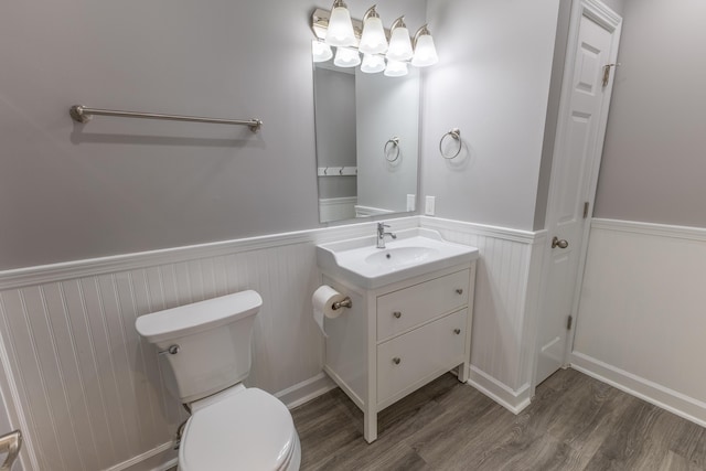 bathroom featuring toilet, wood finished floors, vanity, and wainscoting
