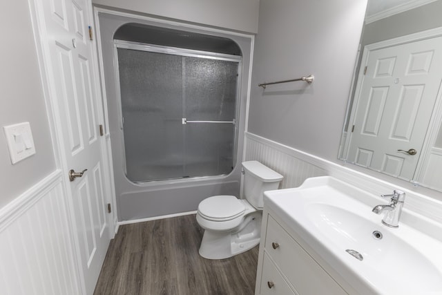bathroom featuring combined bath / shower with glass door, vanity, toilet, a wainscoted wall, and wood finished floors
