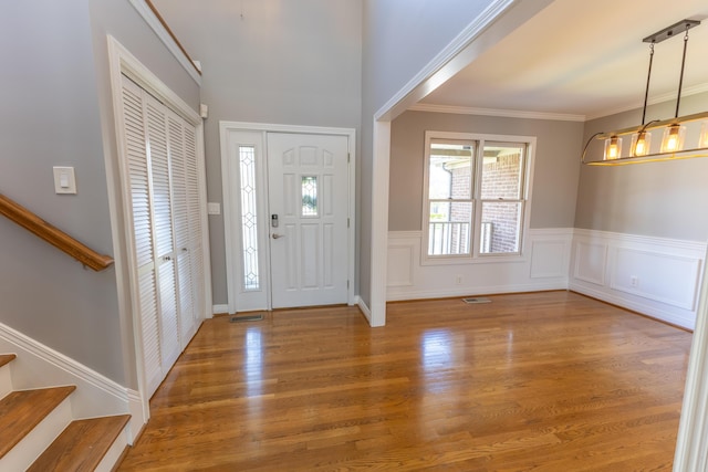 entrance foyer featuring crown molding, a wainscoted wall, stairs, visible vents, and wood finished floors