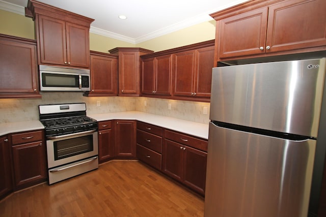 kitchen featuring tasteful backsplash, ornamental molding, light countertops, wood finished floors, and stainless steel appliances