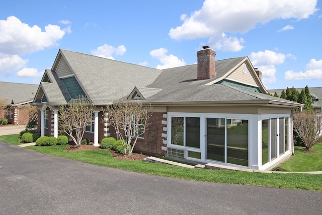 exterior space with brick siding, a chimney, a sunroom, and roof with shingles