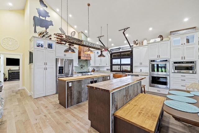 kitchen with butcher block countertops, a center island, backsplash, appliances with stainless steel finishes, and high vaulted ceiling