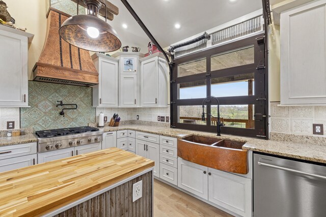 kitchen featuring white cabinets, custom range hood, a sink, stainless steel appliances, and decorative backsplash