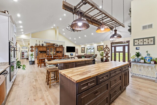 kitchen with visible vents, a center island, light wood finished floors, wood counters, and high vaulted ceiling