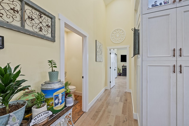 hall featuring light wood-style flooring, a high ceiling, and baseboards