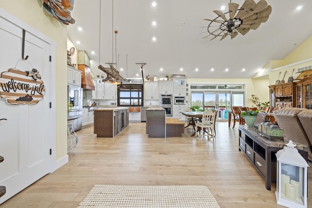 interior space featuring custom exhaust hood, open floor plan, light countertops, a ceiling fan, and a spacious island