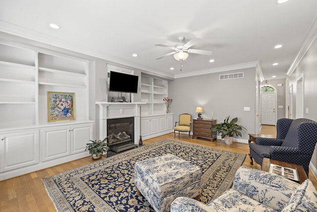 living room with ceiling fan, light wood finished floors, built in features, visible vents, and ornamental molding