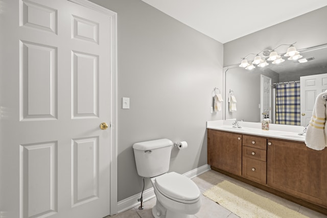 full bath with a sink, double vanity, toilet, tile patterned floors, and baseboards