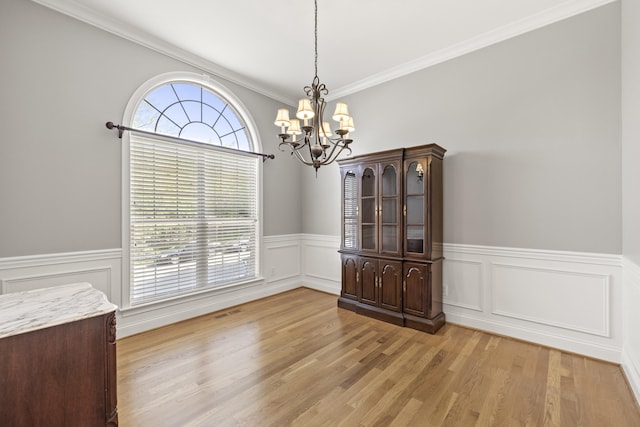 unfurnished dining area featuring an inviting chandelier, ornamental molding, wainscoting, and light wood finished floors