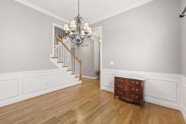 interior space featuring visible vents, crown molding, a wainscoted wall, an inviting chandelier, and stairs