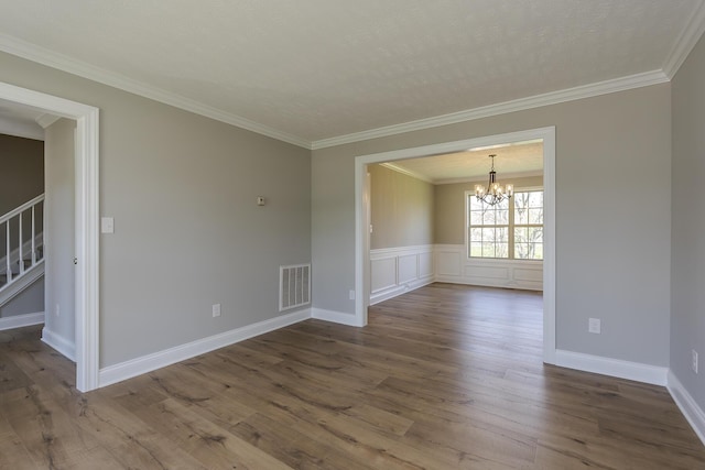 empty room with an inviting chandelier, dark wood finished floors, ornamental molding, visible vents, and stairway