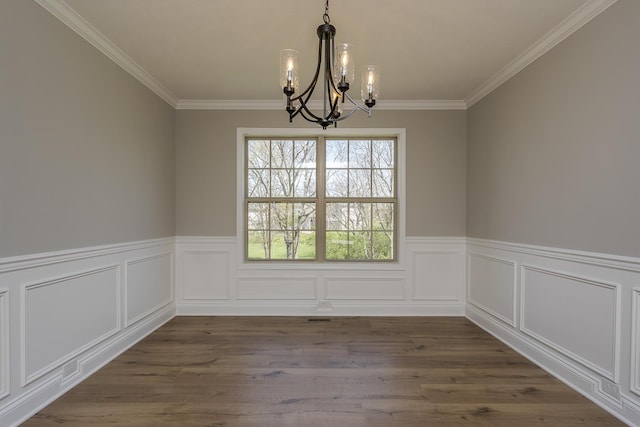 unfurnished dining area with crown molding, a wainscoted wall, an inviting chandelier, and dark wood-style flooring