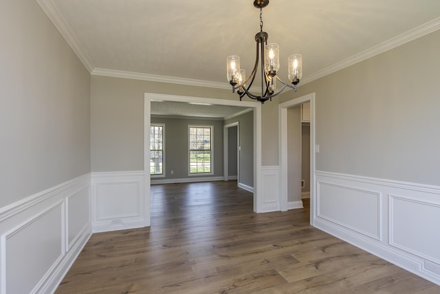 unfurnished dining area with a chandelier, wainscoting, ornamental molding, and wood finished floors