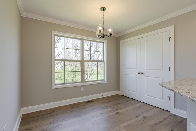 unfurnished dining area featuring crown molding, an inviting chandelier, visible vents, light wood finished floors, and baseboards