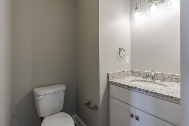 half bathroom featuring toilet, vanity, and baseboards