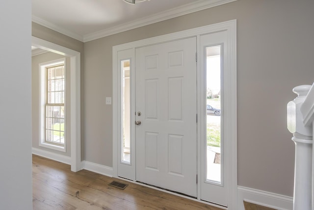 foyer with a healthy amount of sunlight, wood-type flooring, ornamental molding, and visible vents