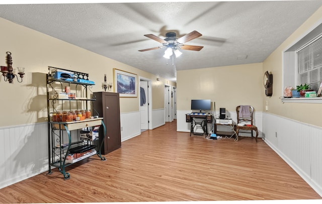 interior space with a ceiling fan, a textured ceiling, wood finished floors, and a wainscoted wall