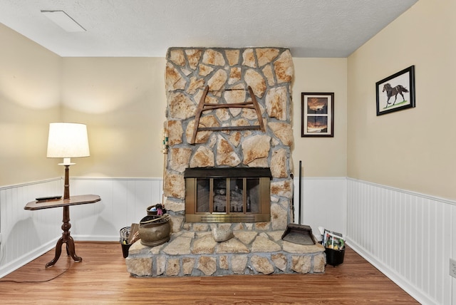 living room with a textured ceiling, a stone fireplace, wood finished floors, and a wainscoted wall