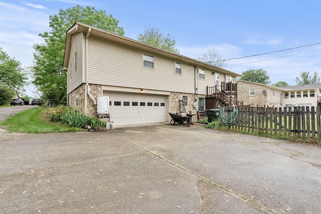 view of front of house with an attached garage, fence, stone siding, and concrete driveway
