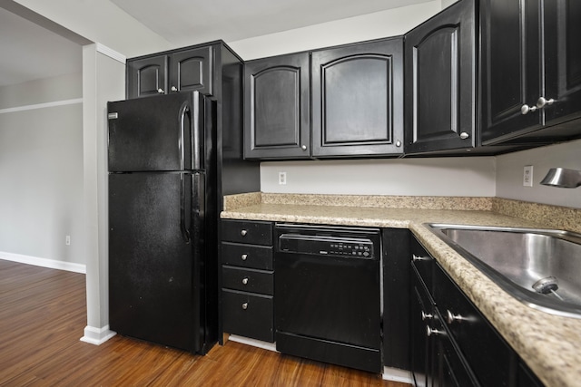 kitchen featuring dark cabinetry, dark wood-style flooring, a sink, and black appliances