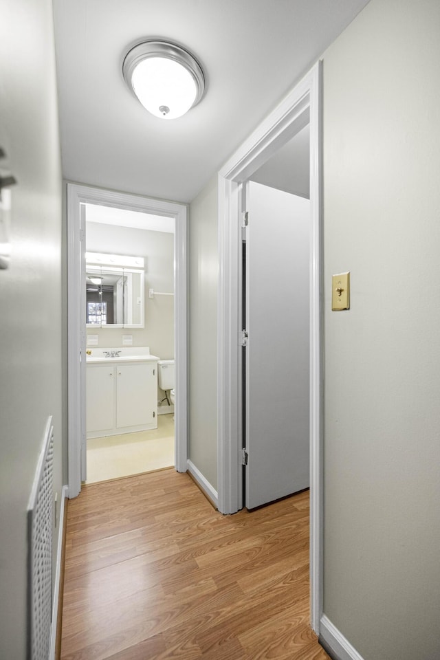 hallway featuring light wood-style flooring, baseboards, and visible vents