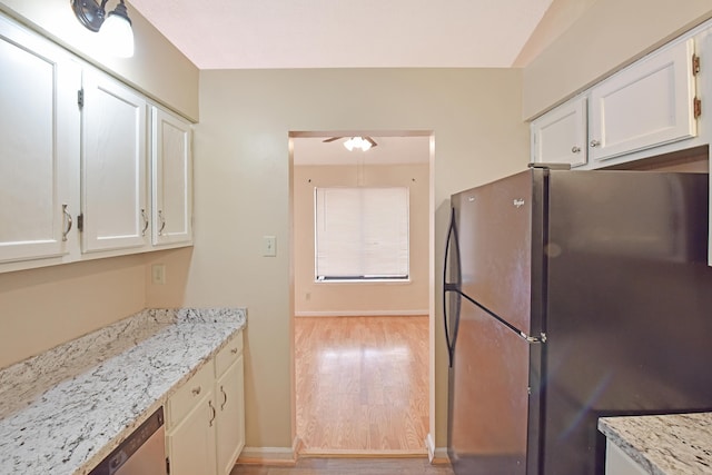 kitchen with light stone counters, a ceiling fan, freestanding refrigerator, white cabinets, and light wood-style floors
