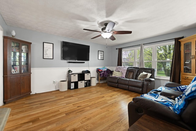 living room featuring a ceiling fan, a textured ceiling, a wainscoted wall, and light wood-style floors
