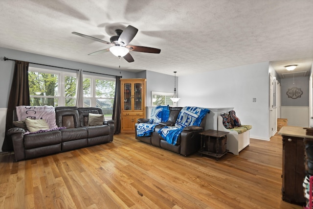 living room featuring ceiling fan, attic access, light wood finished floors, and a textured ceiling