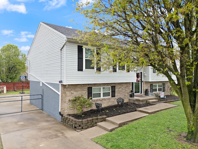 raised ranch with brick siding, fence, and a front lawn