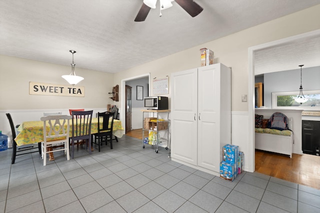 tiled dining area featuring a ceiling fan and a wainscoted wall