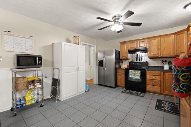 kitchen with dark countertops, under cabinet range hood, a ceiling fan, appliances with stainless steel finishes, and light tile patterned floors