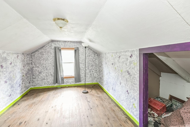 additional living space with baseboards, vaulted ceiling, hardwood / wood-style flooring, and wallpapered walls