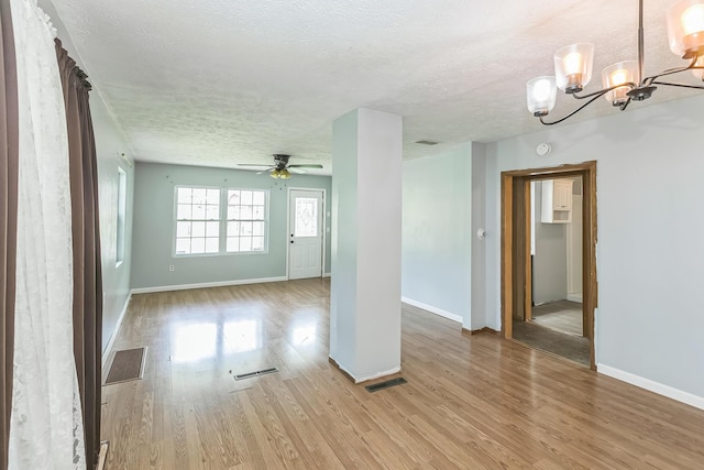 empty room with light wood-style flooring, a textured ceiling, baseboards, and visible vents