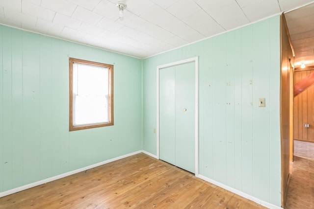 unfurnished bedroom with a closet, baseboards, hardwood / wood-style floors, and wood walls