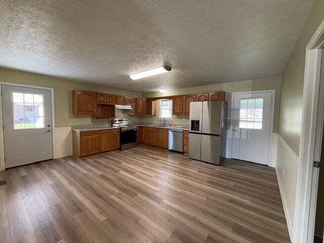 kitchen with light countertops, a wealth of natural light, a textured ceiling, wood finished floors, and stainless steel appliances