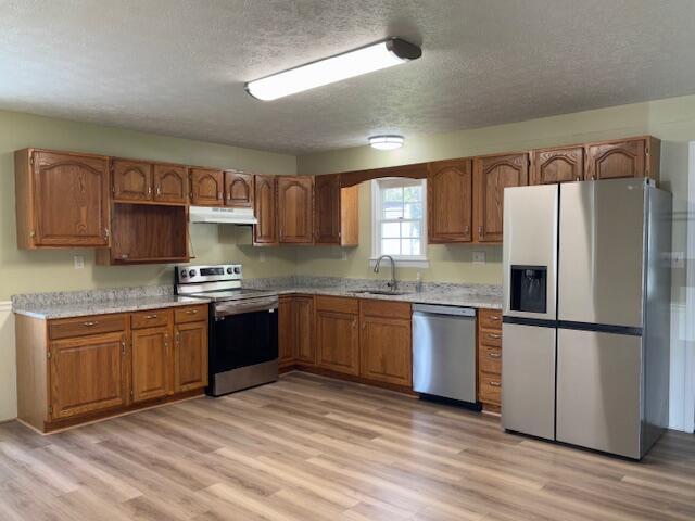 kitchen with a textured ceiling, appliances with stainless steel finishes, light wood-type flooring, and under cabinet range hood