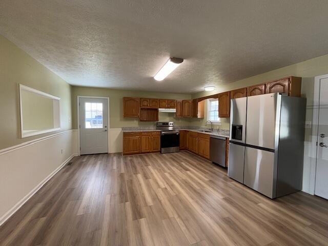 kitchen with a sink, light countertops, light wood-type flooring, a textured ceiling, and stainless steel appliances