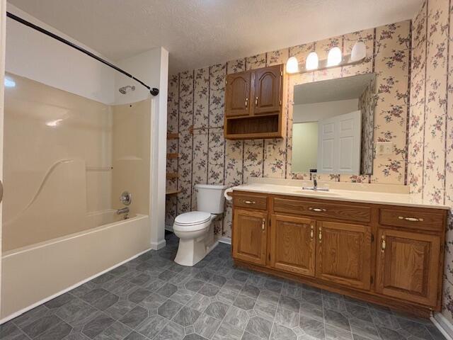 full bathroom featuring toilet, wallpapered walls, vanity, and  shower combination
