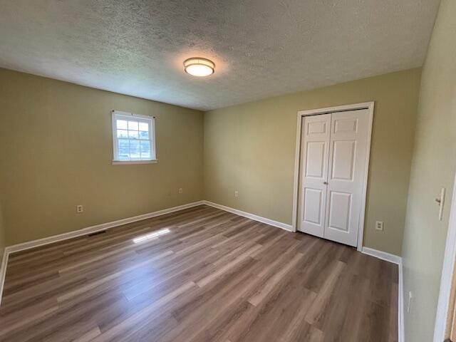 unfurnished bedroom featuring baseboards, a closet, a textured ceiling, and wood finished floors