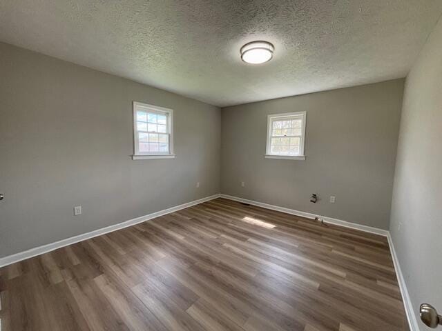 empty room with a textured ceiling, wood finished floors, and baseboards