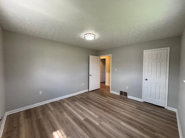unfurnished bedroom with a textured ceiling, wood finished floors, baseboards, and visible vents