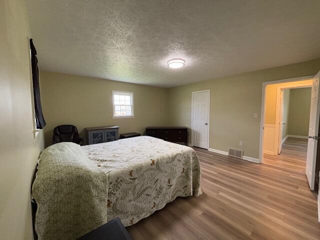 bedroom featuring visible vents, a textured ceiling, baseboards, and wood finished floors