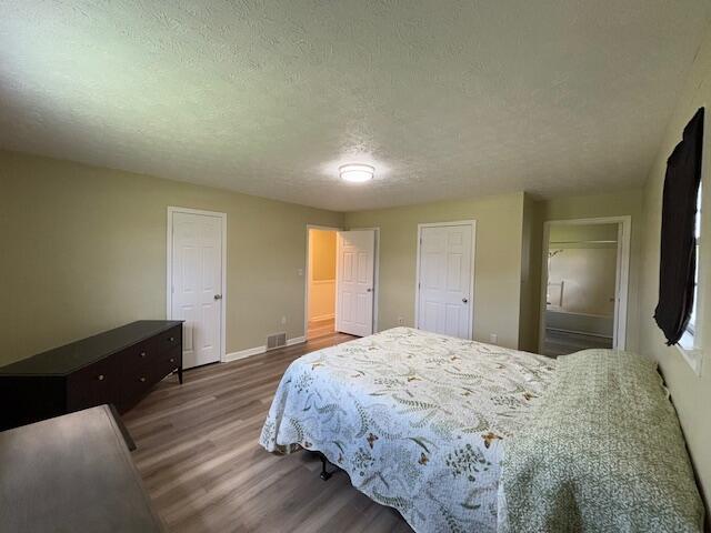 bedroom featuring visible vents, a textured ceiling, baseboards, and wood finished floors